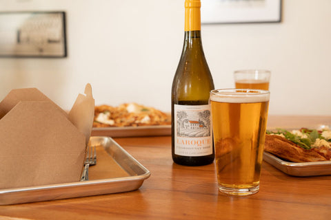Bottle of wine and a glass of beer on a table with food in the background