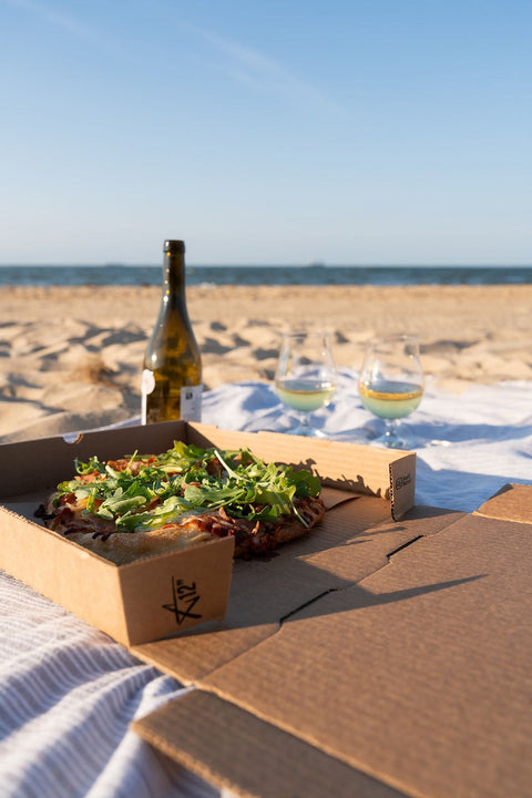 Box of pizza with salad on a beach setting
