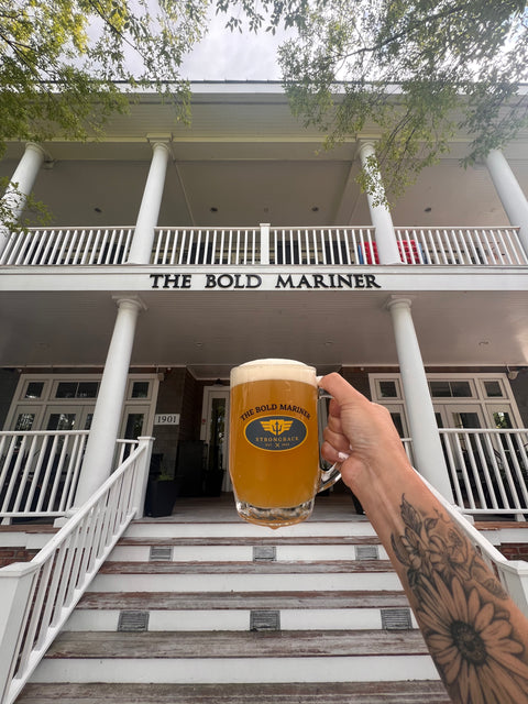 Person holding a beer mug with 'The Bold Mariner Strongback Mug' logo in front of a building named 'The Bold Mariner'.