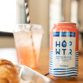 Can of Hop WTR sparkling hop water on a table with a glass of pink drink and pastry.