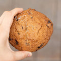 Hand holding a large chocolate chip cookie with a blurred background