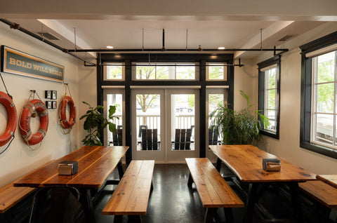 Modern interior with wooden tables and benches, large windows, and decorative life rings on the wall.
