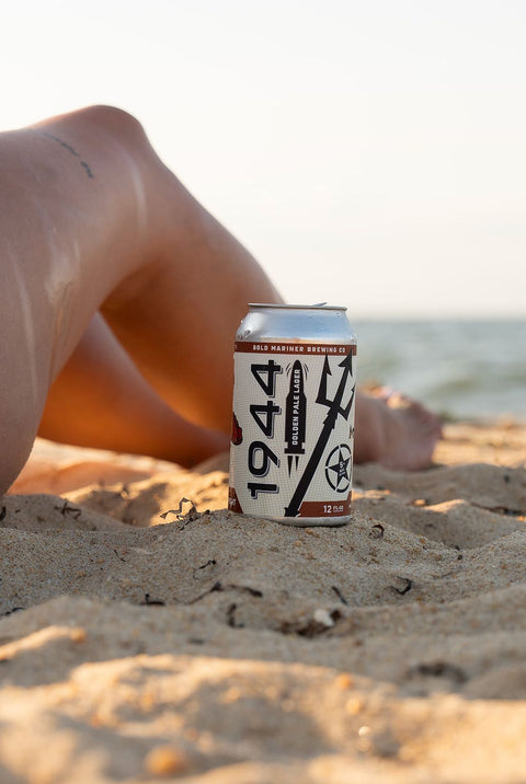 1944 beer can on a sandy beach with blurred legs in the background
