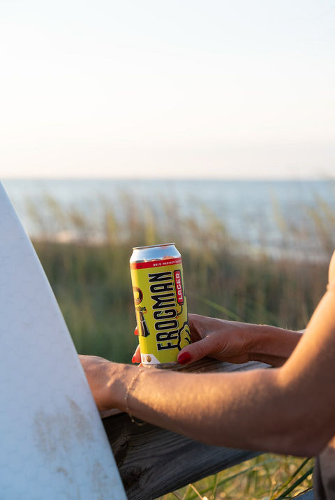 Person holding a can of Frogman lager outdoors with grass and sky in the background