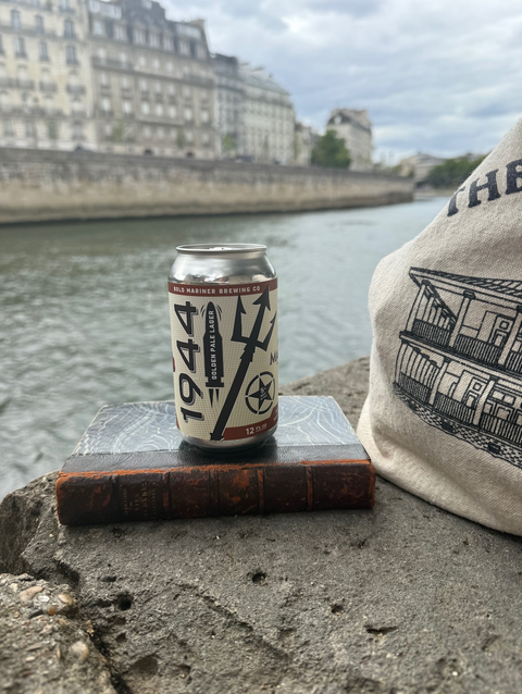 Can of 1944 golden pale lager on a book with a cityscape and river in the background in London
