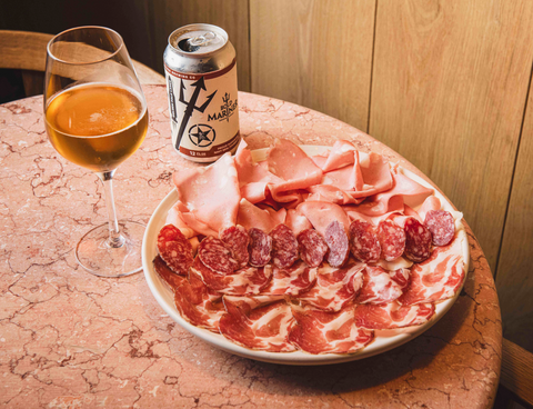 Platter of cured meats with a glass of Bold Mariner beer and can on a wooden table.