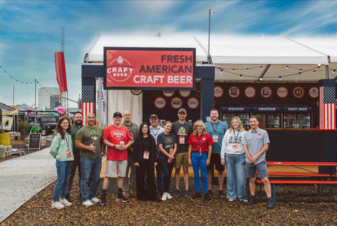 Group of people posing in front of a 'Fresh American Craft Beer' booth at an outdoor event.