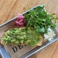 Avocado toast with arugula and pickled onions on a metal tray.