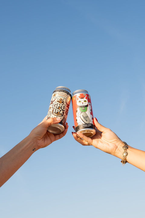 Two cans of beer held up against a clear blue sky