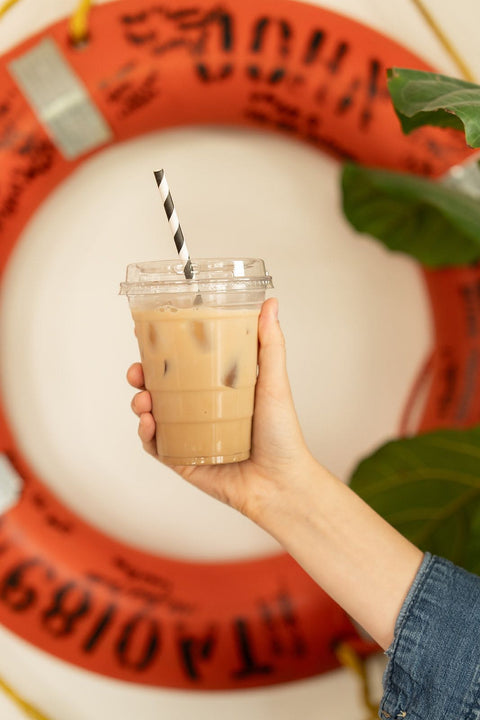 Hand holding a cup of iced coffee with a straw against a decorative background