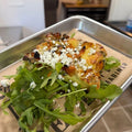 Plated quiche dish with roasted vegetables on a bed of arugula in a kitchen setting.