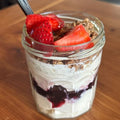 Yogurt in a jar with strawberries and a spoon on a wooden surface