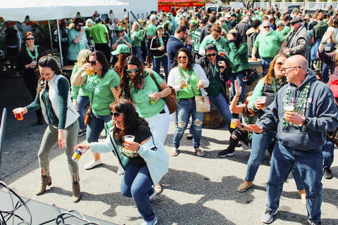 Group of people in green shirts at a St. Patrick's Day event, drinking beer.