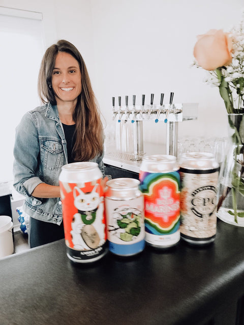 Woman standing behind a bar with colorful beer cans on the counter at Bold Mariner Brewery