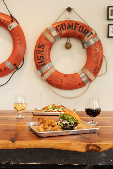 Dining setup with food and drinks on a wooden table, lifebuoys on the wall.