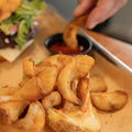 Fries on a plate with a side of ketchup, a burger in the background.