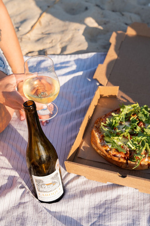 Person enjoying a pizza and wine on a beach with a bottle of white wine and a box of pizza on beach in Virginia Beach