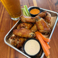 Tray of chicken wings with dipping sauces, carrots, celery, and a glass of beer on a wooden table.