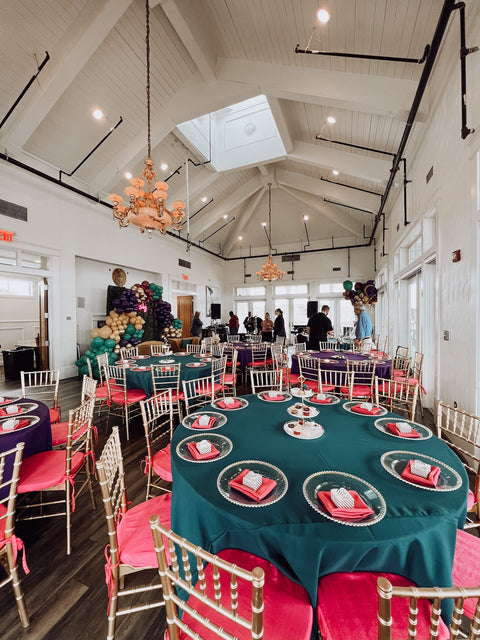 Event venue with tables set for a gathering, featuring teal tablecloths and pink chairs.