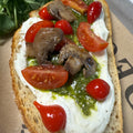 Open-faced sandwich with tomatoes, mushrooms, and pesto on a rustic bread slice.