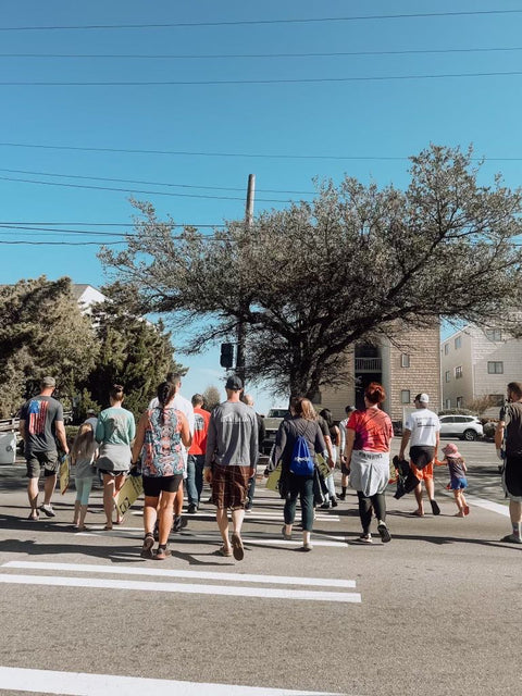 Group of people crossing a street at a crosswalk with trees and buildings in the background.