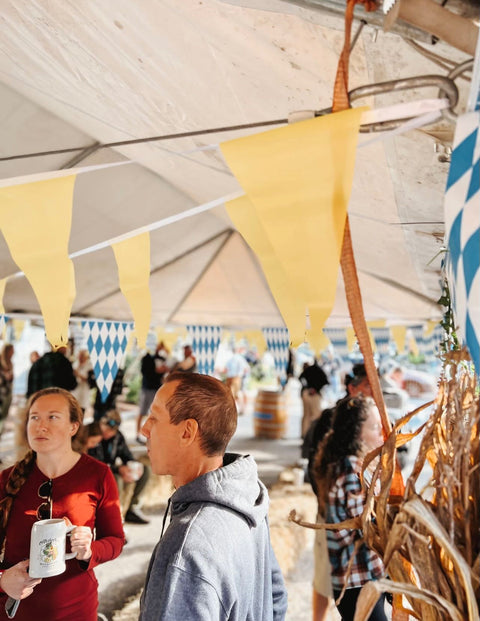 People at an outdoor event with yellow flags and a wooden structure.