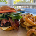 Hamburger with bacon and cheese next to fries on a plate outdoors.