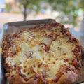 Cheesy pizza on a metal tray with a blurred outdoor background