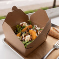 Salad in a cardboard container on a table with a fork, outdoors.