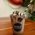 Iced Mocha drink in a clear cup with whipped cream, placed on a wooden surface with a decorative life buoy in the background.
