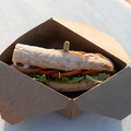 Sandwich in a cardboard box on a white surfboard