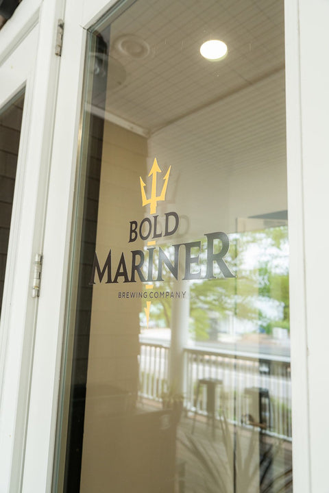 Glass door with 'Bold Mariner Brewing Company' logo reflected on a sunny day.