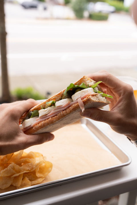 Two hands splitting a sandwich with chips on a tray.