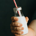 Hand holding glass of milk with straw