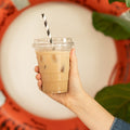 Hand holding a cup of iced coffee with a straw against a decorative background